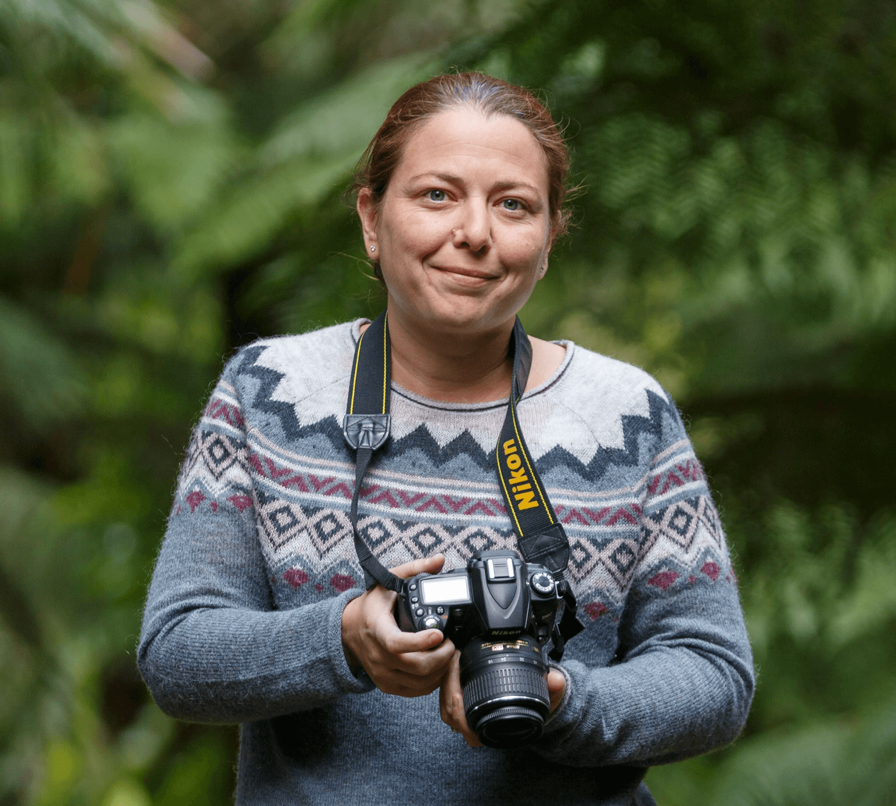 A-woman-wearing-a-knitted-sweater-in-a-ranforest-holding-a-professional-camera