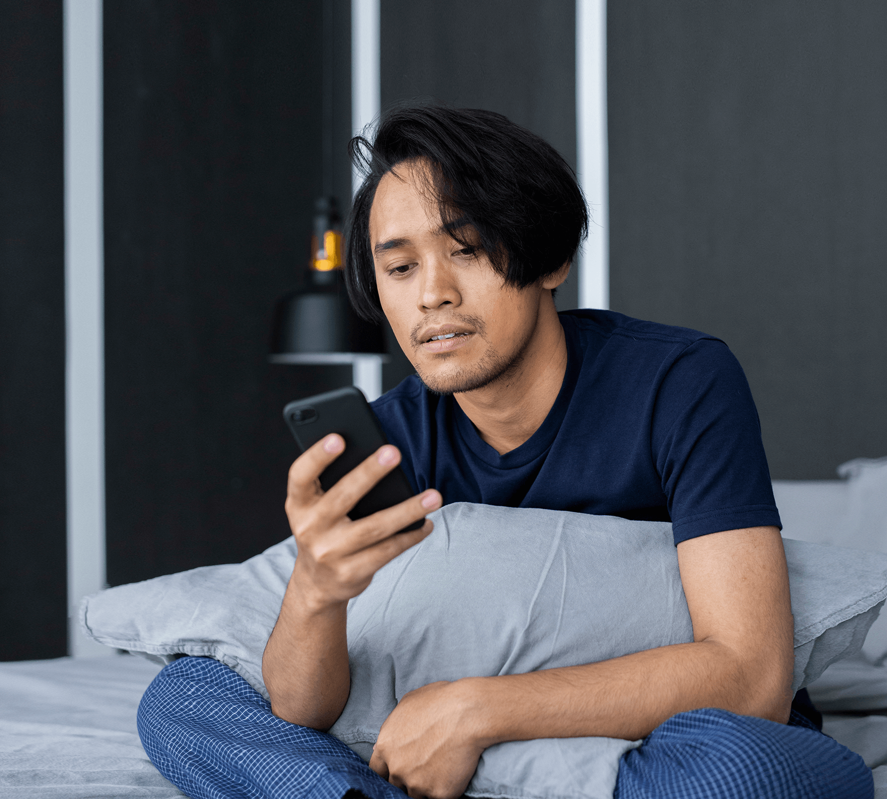 A-man-sitting-on-his-bed-looking-at-his-mobile-phone