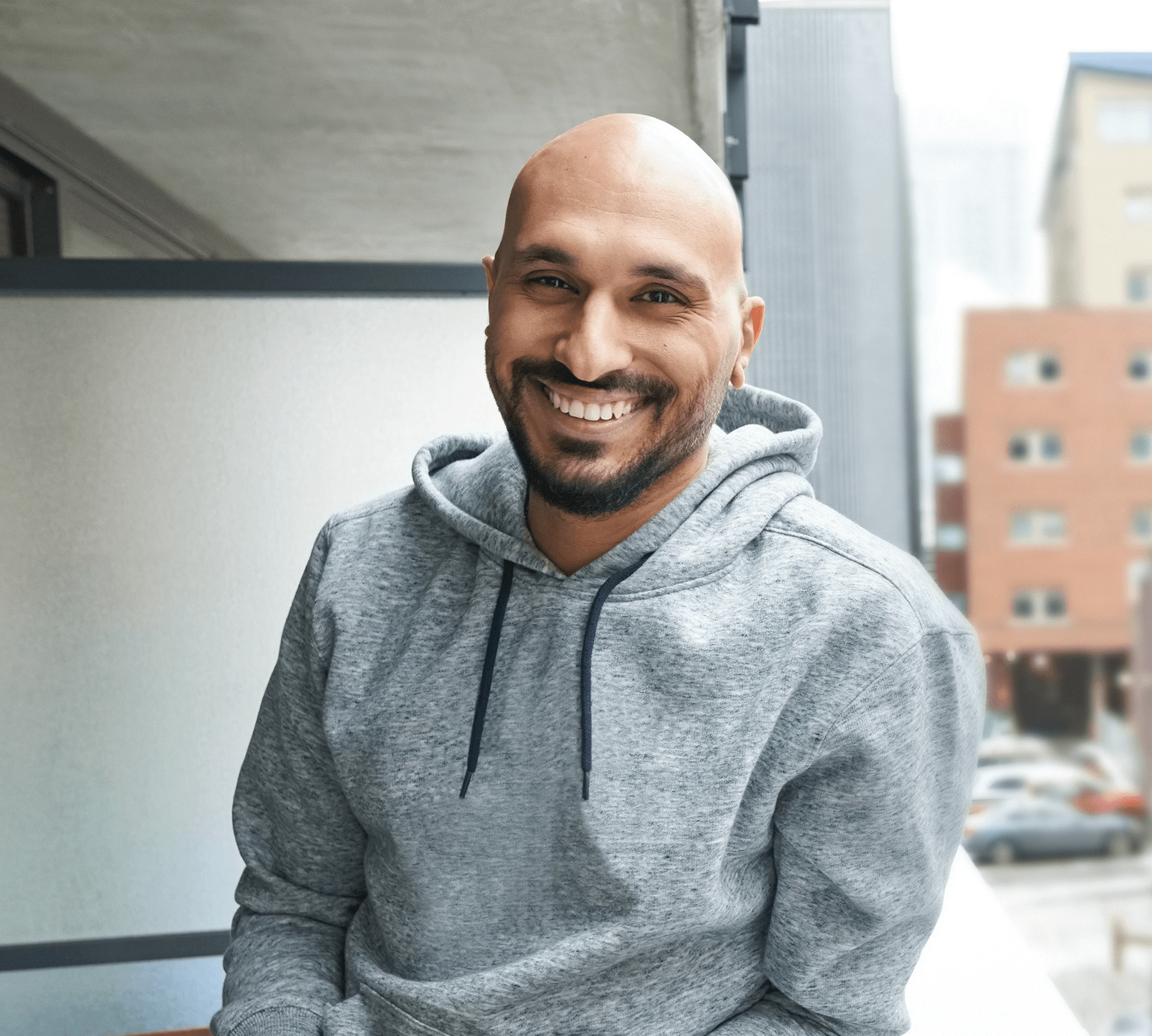 A-man-with-a-shaved-head-and-short-beard-leaning-on-a-balcony-railing-smiling